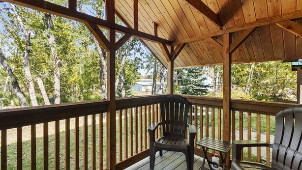 A covered outdoor deck with wooden railings, two Adirondack chairs, and a small table. - Château Rouge 213 ~ Grizzly Peak Getaway (Red Lodge)