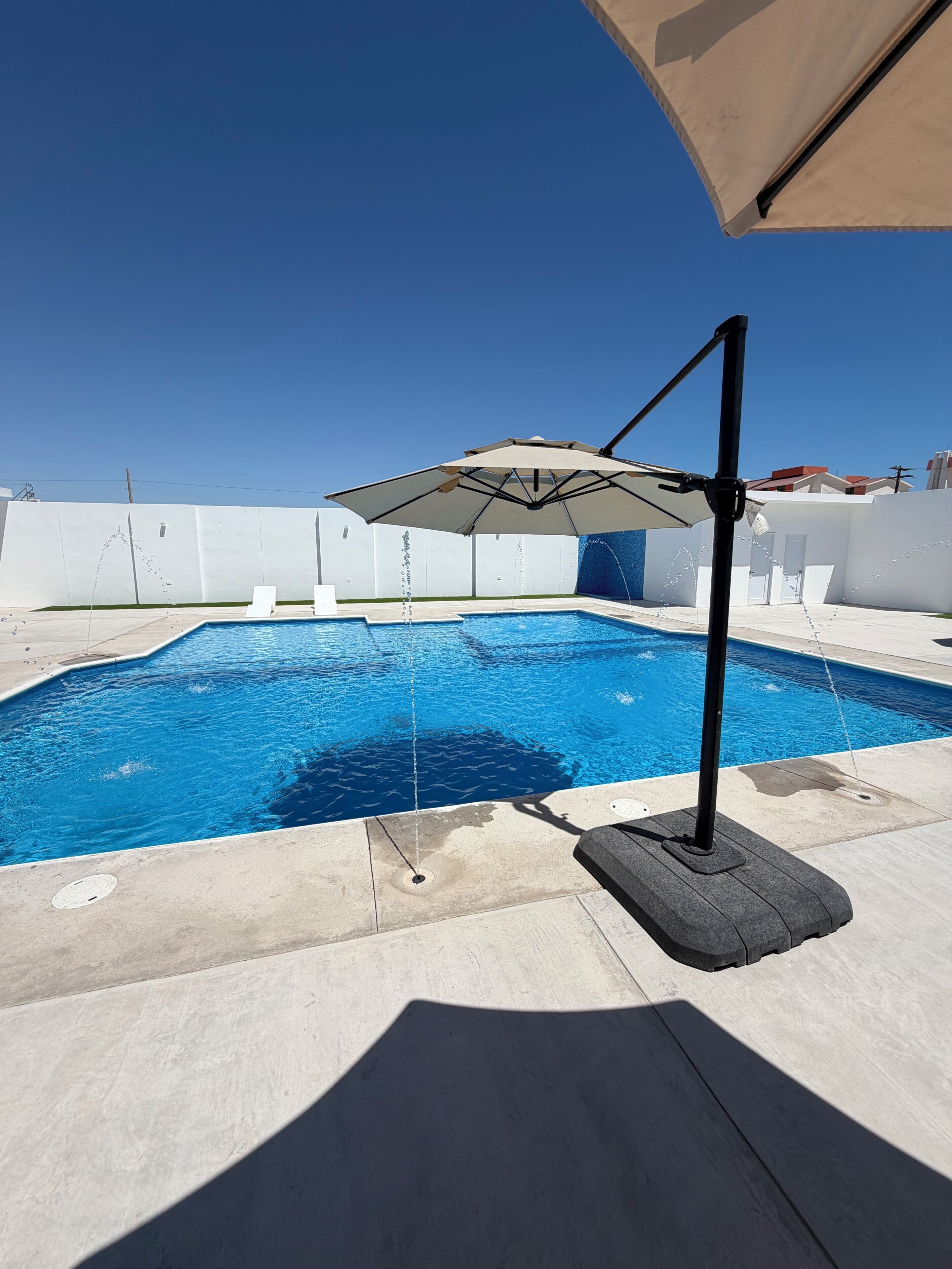 Una piscina con fuente, una silla de descanso y una sombrilla.