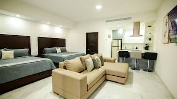 Une chambre d’hôtel moderne équipée de deux lits simples, d’un canapé, d’un bureau et d’un coin cuisine.