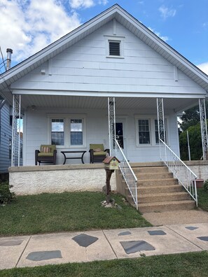 A white two-story house with a covered porch, a small window, and a set of stairs leading to the front door.