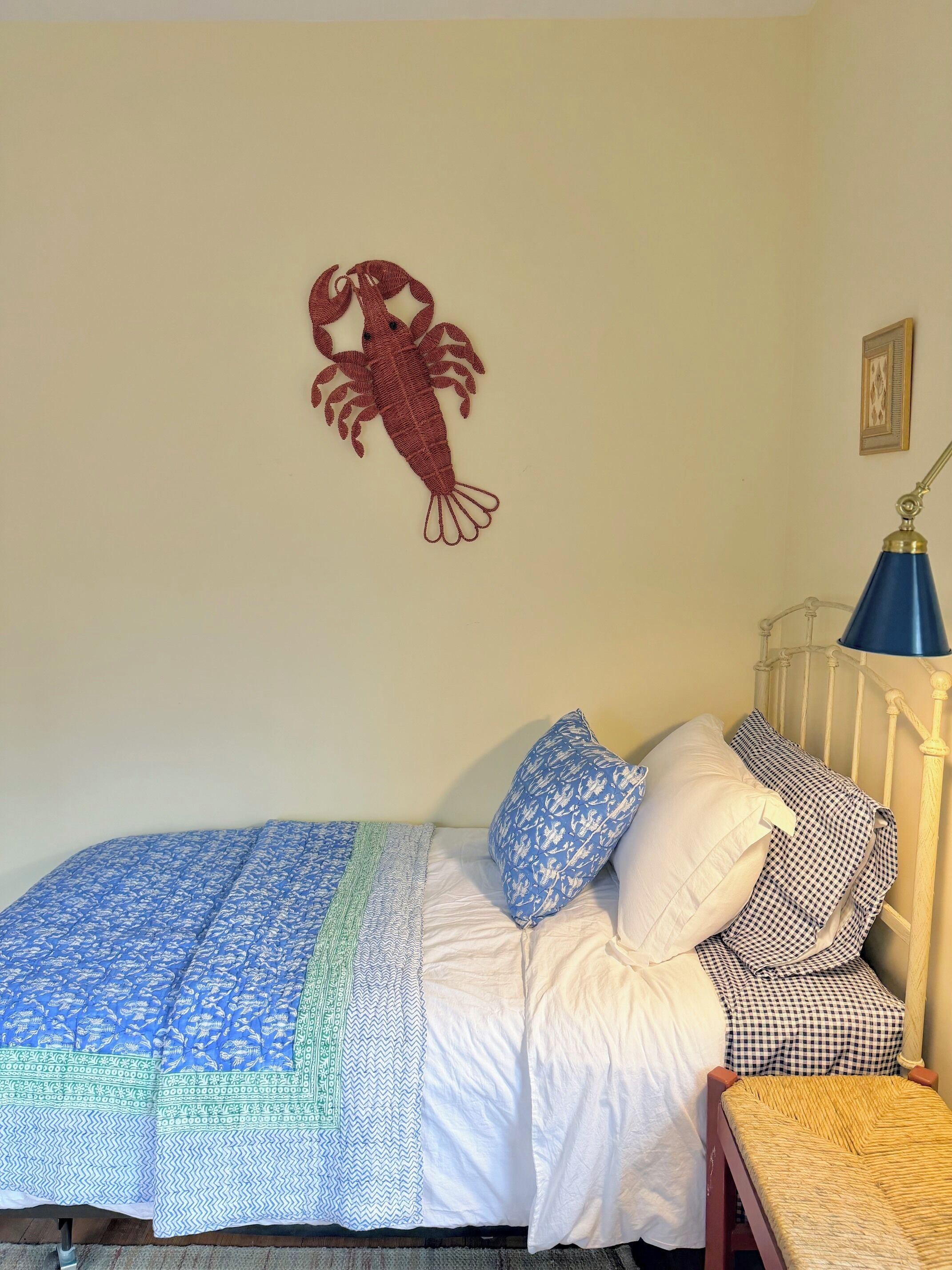 A bed with a blue patterned bedspread, white pillows, and a blue lamp on a white metal bed frame.