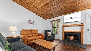 A living room with a leather sofa, a wooden coffee table, a fireplace, and a TV mounted on the wall.
