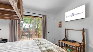 A bedroom with a large bed, a wooden bench, a sliding glass door to a balcony, and a sign for RENTBRANSON.COM.