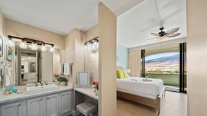 Un baño moderno con un espejo grande, tocador y ducha. La habitación doble tiene una cama, mesita de noche y vistas al exterior.