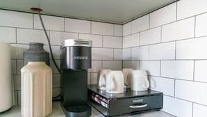 Ett kök med en Keurig-kaffemaskin, en behållare för kaffekapslar och flera vita kaffemuggar på en bänkskiva.