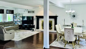 A modern living room with a sofa, TV, fireplace, dining table, and chandelier.