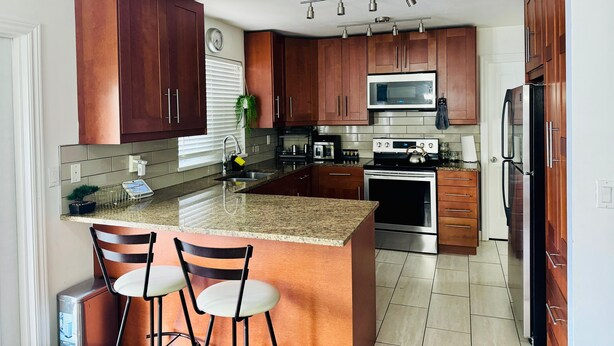 A modern kitchen with wooden cabinets, stainless steel appliances, a granite countertop, and a built-in island with bar stools.