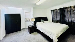 A bedroom with a bed, a nightstand, a lamp, a window with blinds, and a ceiling light.