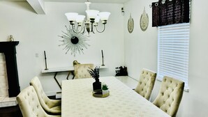 A dining area with a chandelier, a patterned tablecloth, and tufted chairs.