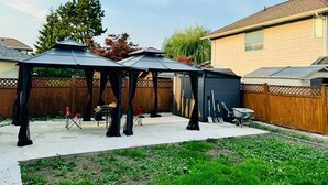 A backyard with two gazebos, a wooden fence, and a shed.