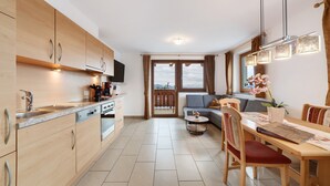 A modern kitchen with wooden cabinets, a dining area with a table and chairs, and a view through a glass door to an outdoor balcony. - Apartment 'Adlerhorst' with Mountain View, Shared Garden and Wi-Fi (Lagundo)