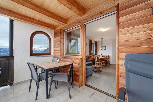 A wooden interior with a dining area, a sofa, and a view of the mountains.