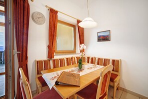 A dining area with a wooden table, bench seating, a clock, a window with curtains, and a small vase with flowers. - Apartment 'Storchennest' with Mountain View, Shared Garden and Wi-Fi (Lagundo)