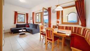 A living room with a sofa, a dining table, and chairs, a window with curtains, and a view of the outdoors. - Apartment 'Storchennest' with Mountain View, Shared Garden and Wi-Fi (Lagundo)
