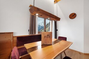 Een houten eettafel met een houten doos, gewatteerde banken en een klok aan de muur.