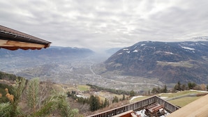 Panoramisch uitzicht vanaf een balkon over een vallei met bergen, een stad en een rivier.