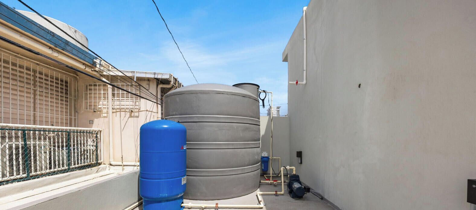 A narrow alley with water tanks and a blue gas cylinder.