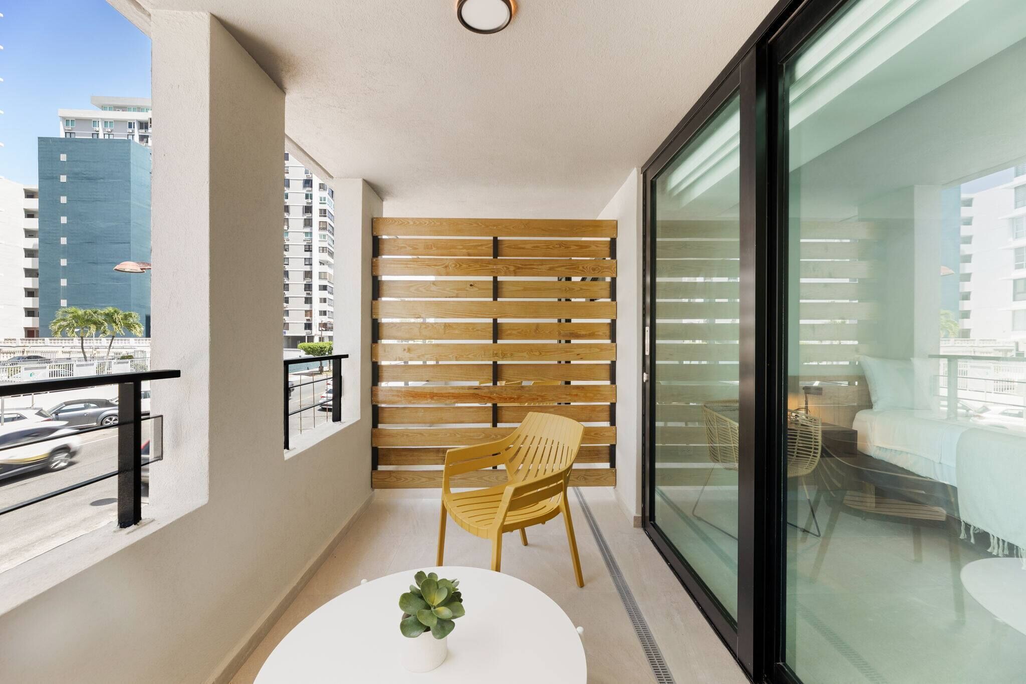 Ein Balkon mit einer Holzlamellenwand, einem runden Tisch mit einem Topfblumenbeet und einem Stuhl.