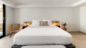 A modern bedroom with a large bed, two bedside tables with lamps, a wicker chair, and a small plant. - Isla Verde Ocean View | Entire 2nd Floor Suite (San Juan)