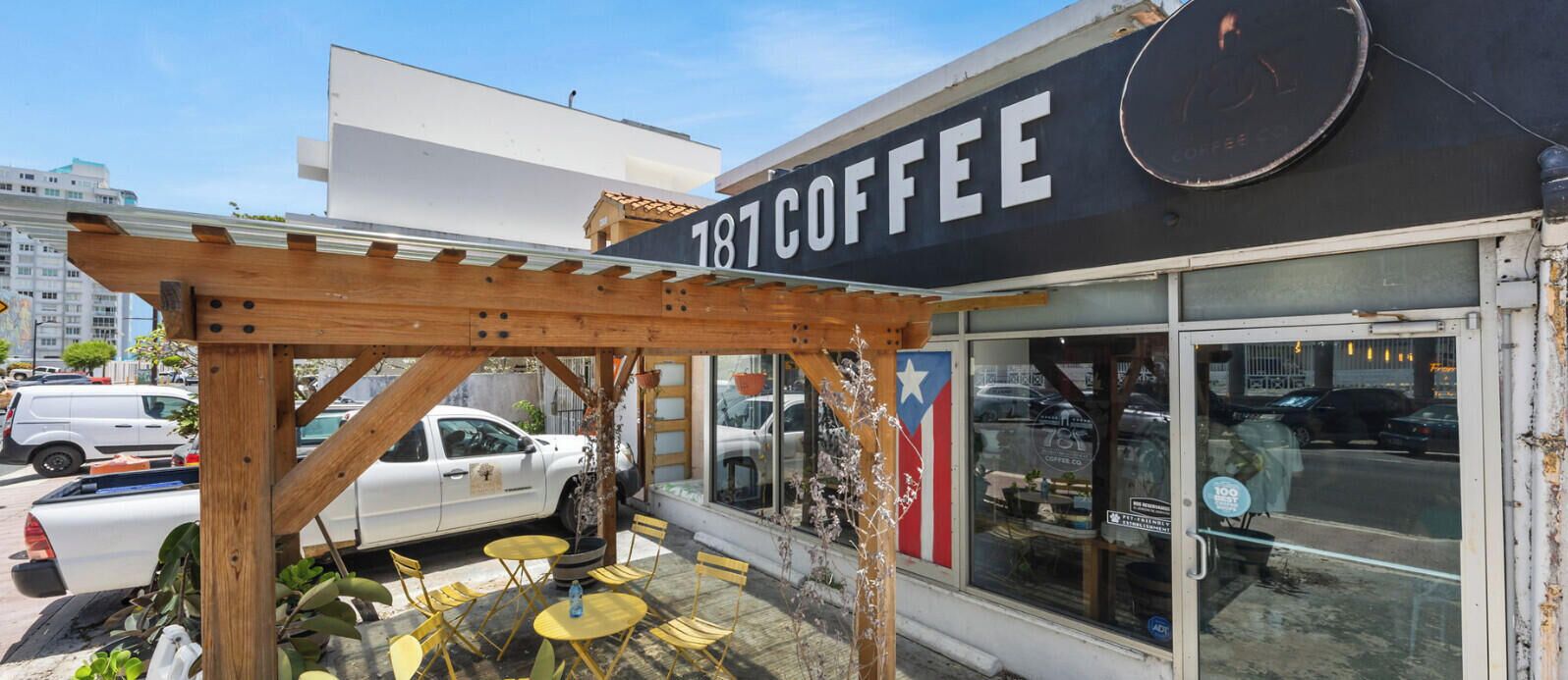 A coffee shop with outdoor seating, a wooden pergola, and a large sign displaying '181 COFFEE'.