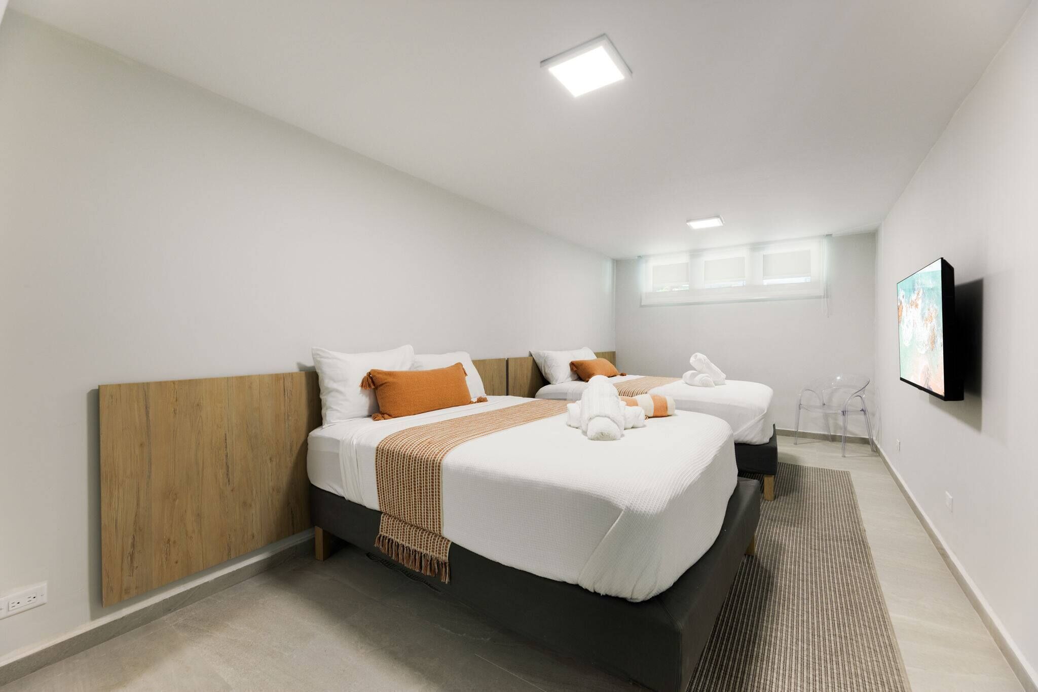 Camera d'albergo con un letto grande, due letti più piccoli, una testiera in legno, biancheria bianca, una coperta marrone, un asciugamano bianco, una TV a schermo piatto e una finestra con tende.