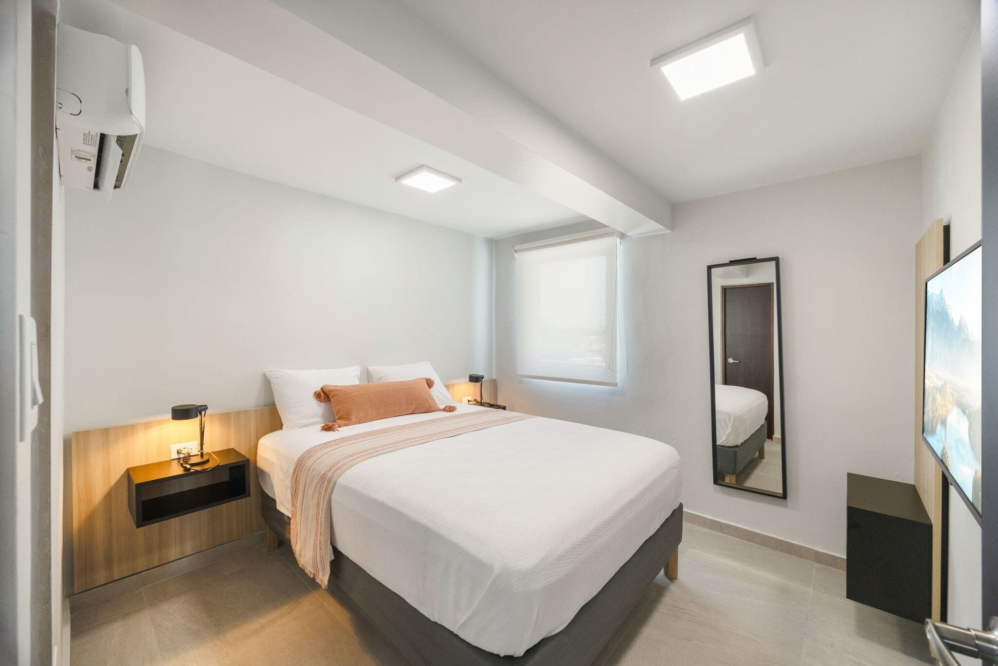 Een moderne hotelkamer met een groot bed, nachtkastjes, een spiegel en een televisie.