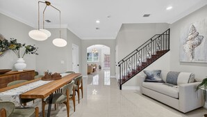 A spacious living area with a wooden dining table, a sofa, and a staircase. - Daisy Townhouse  Steps from The Beach (Pompano Beach)