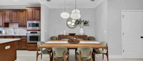 A modern kitchen with wooden cabinets, stainless steel appliances, and a dining area with a wooden table and green chairs.
