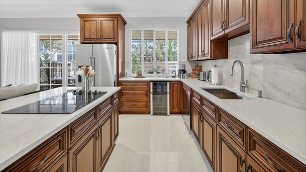 A modern kitchen with wooden cabinets, a large island, stainless steel appliances, and a view of the outdoors. - Daisy Townhouse  Steps from The Beach (Pompano Beach)