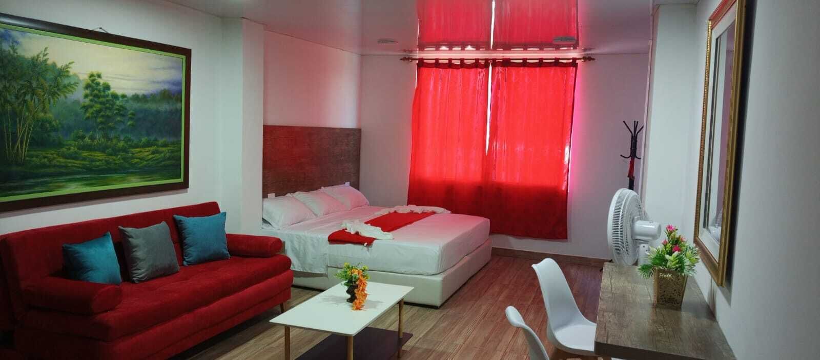 A compact bedroom with a bed, a red sofa, a white coffee table, and a painting on the wall.