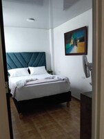 A bedroom with a bed, a headboard, a wall-mounted fan, and a painting.