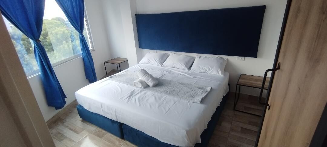 A neatly made bed with white linens and pillows, a dark blue headboard, and a small bedside table with a lamp.