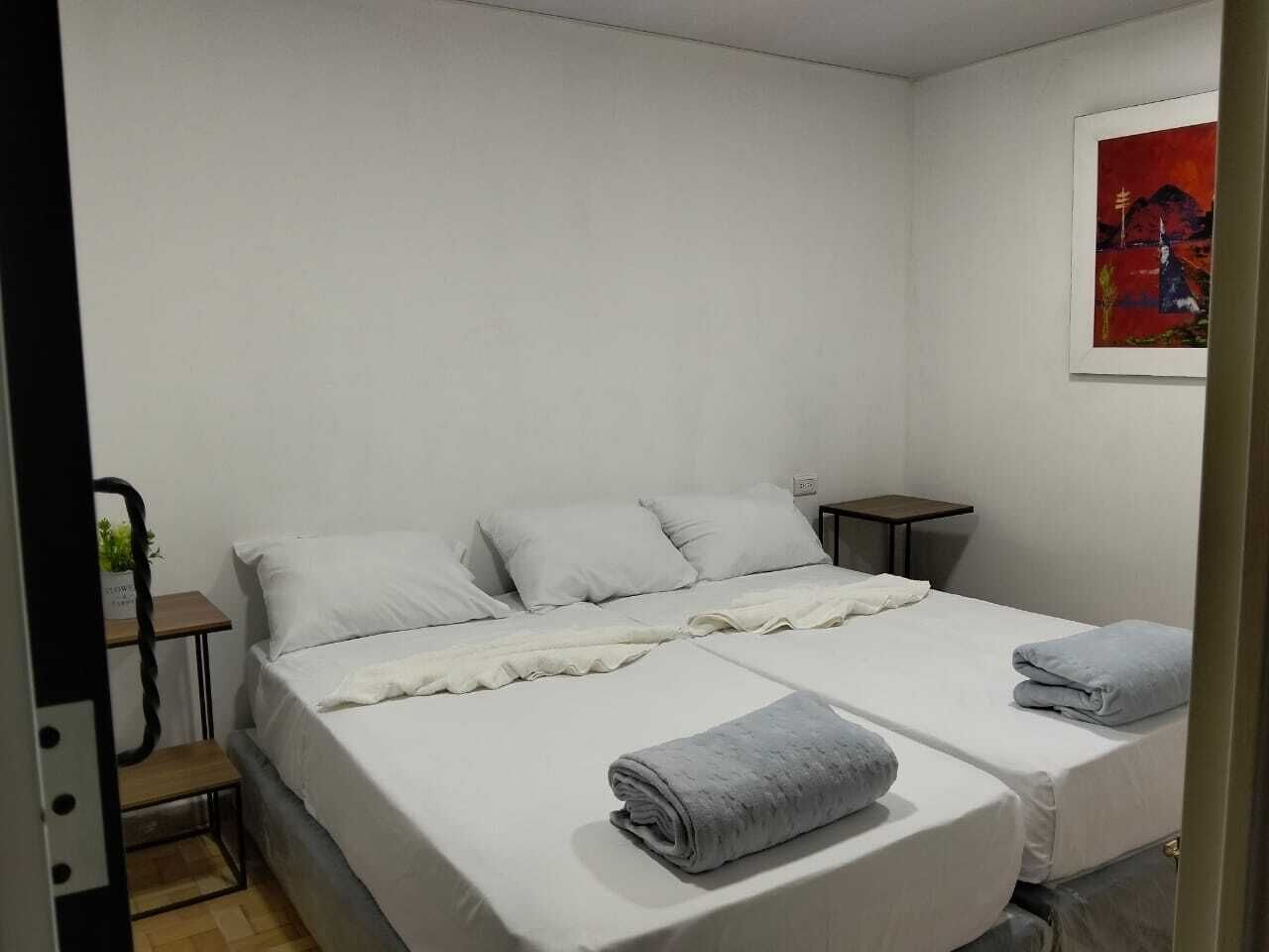 Un letto matrimoniale con lenzuola bianche, un comodino e un quadro appeso al muro.