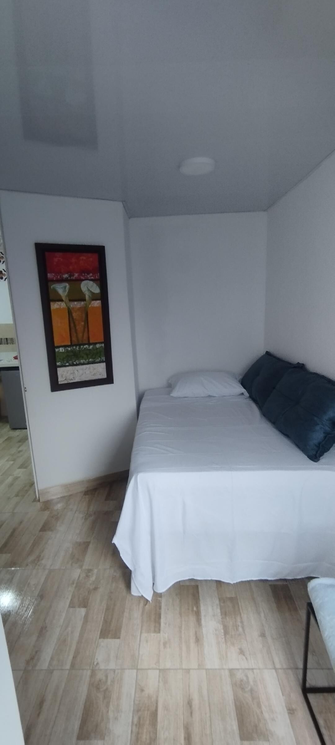 A small, neatly arranged bedroom with a bed, pillows, and a framed picture on the wall.