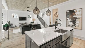 A modern kitchen with a large island, pendant lights, and a staircase leading to a loft area. - 2 Homes in Inlet Beach by Avantstay Dock+lake Access, Saltwater Pool, Close to the Beach (Panama City Beach)