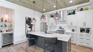 A modern kitchen with white cabinetry, a central island with bar stools, pendant lighting, and a stainless steel oven. - 2 Homes in Inlet Beach by Avantstay Dock+lake Access, Saltwater Pool, Close to the Beach (Panama City Beach)