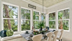 A dining area with a table set for four, large windows, and a view of trees and greenery outside. - 2 Homes in Inlet Beach by Avantstay Dock+lake Access, Saltwater Pool, Close to the Beach (Panama City Beach)