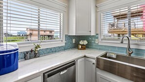 A kitchen with white cabinets, a stainless steel sink, and a window with blinds. - SAN LUIS BEACH GEM - Bay & Gulf Views, Boat launch access, Short Walk to Beach (Freeport)
