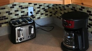 Eine Küche mit einem Toaster und einer Kaffeemaschine auf der Arbeitsfläche, einer gefliesten Spritzschutzwand und Holzschränken.