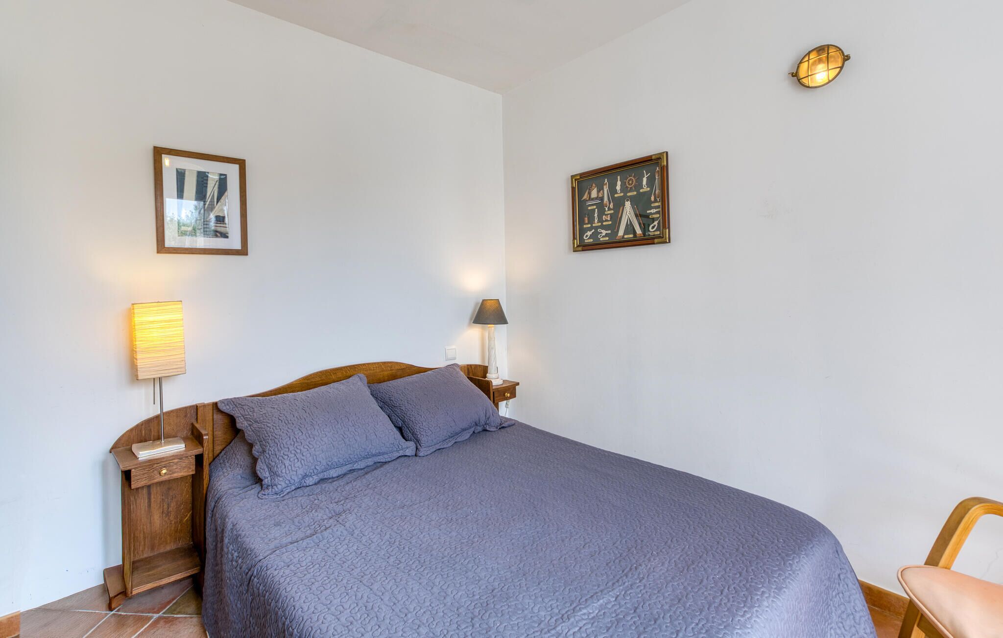 A bedroom with a bed, two bedside lamps, a nightstand, and two framed pictures on the wall.