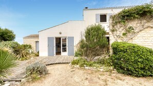 A two-story house with a wooden deck, a stone wall, and a variety of plants and shrubs. - Gorgeous home in Saint-Pierre-d'Oléron with WiFi (Saint-Pierre-d'Oléron)