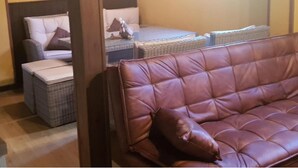 Un sofá de cuero marrón en una habitación con muebles de mimbre y una mesita con un peluche.