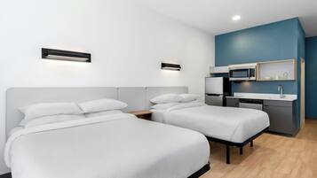 Ein modernes Hotelzimmer mit zwei Betten, einer Küchenzeile und einem kleinen Schreibtisch.