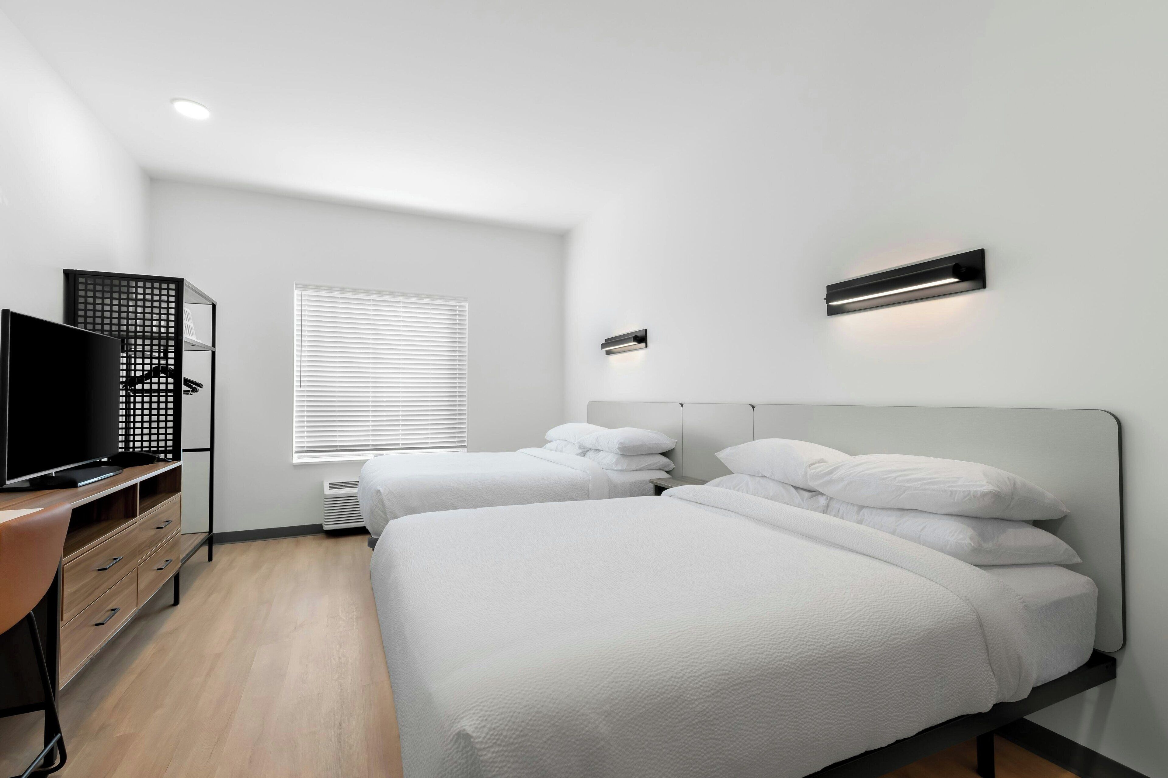 Una habitación de hotel moderna con dos camas, un escritorio y un televisor.