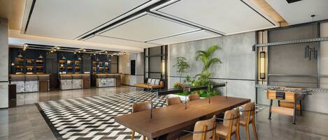 A modern hotel lobby with a large wooden reception desk, seating area, and a foosball table.