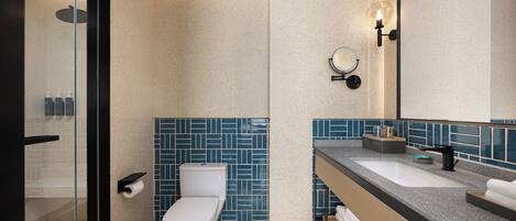 Ein modernes Badezimmer mit Duschkabine aus Glas, einer weißen Toilette und einem Waschtisch mit Waschbecken und Spiegel.