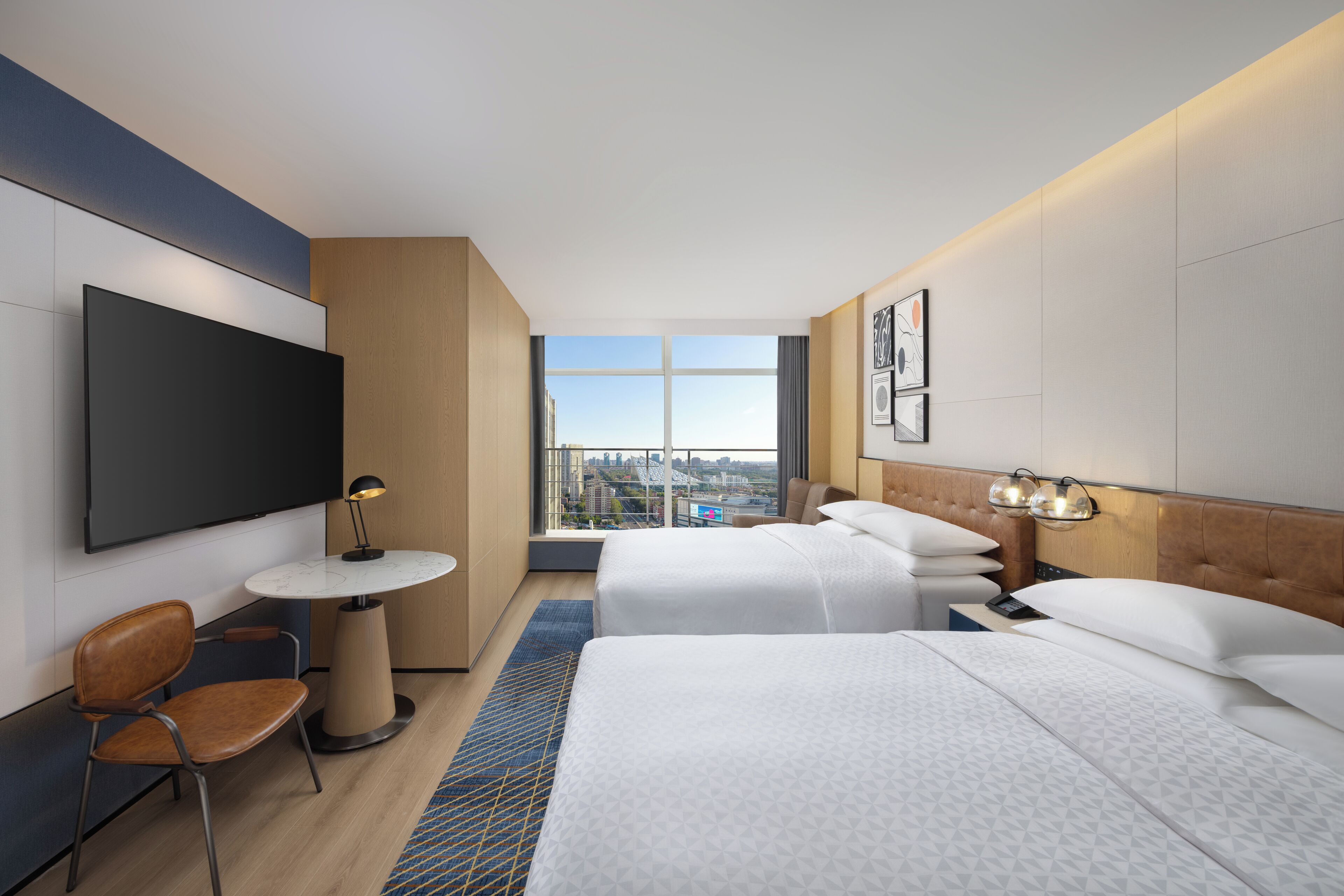 A hotel room with two beds, a TV, a desk, and a view of the city.