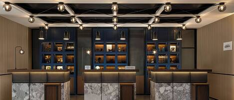 A hotel reception area with three counters, each with a marble top and a wooden base. Overhead, there are multiple pendant lights.