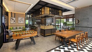 A modern hotel lobby with a foosball table, a bar area, and a dining space with a large wooden table and chairs. - Four Points By Sheraton Beijing Sanlitun Workers Stadium (Beijing)