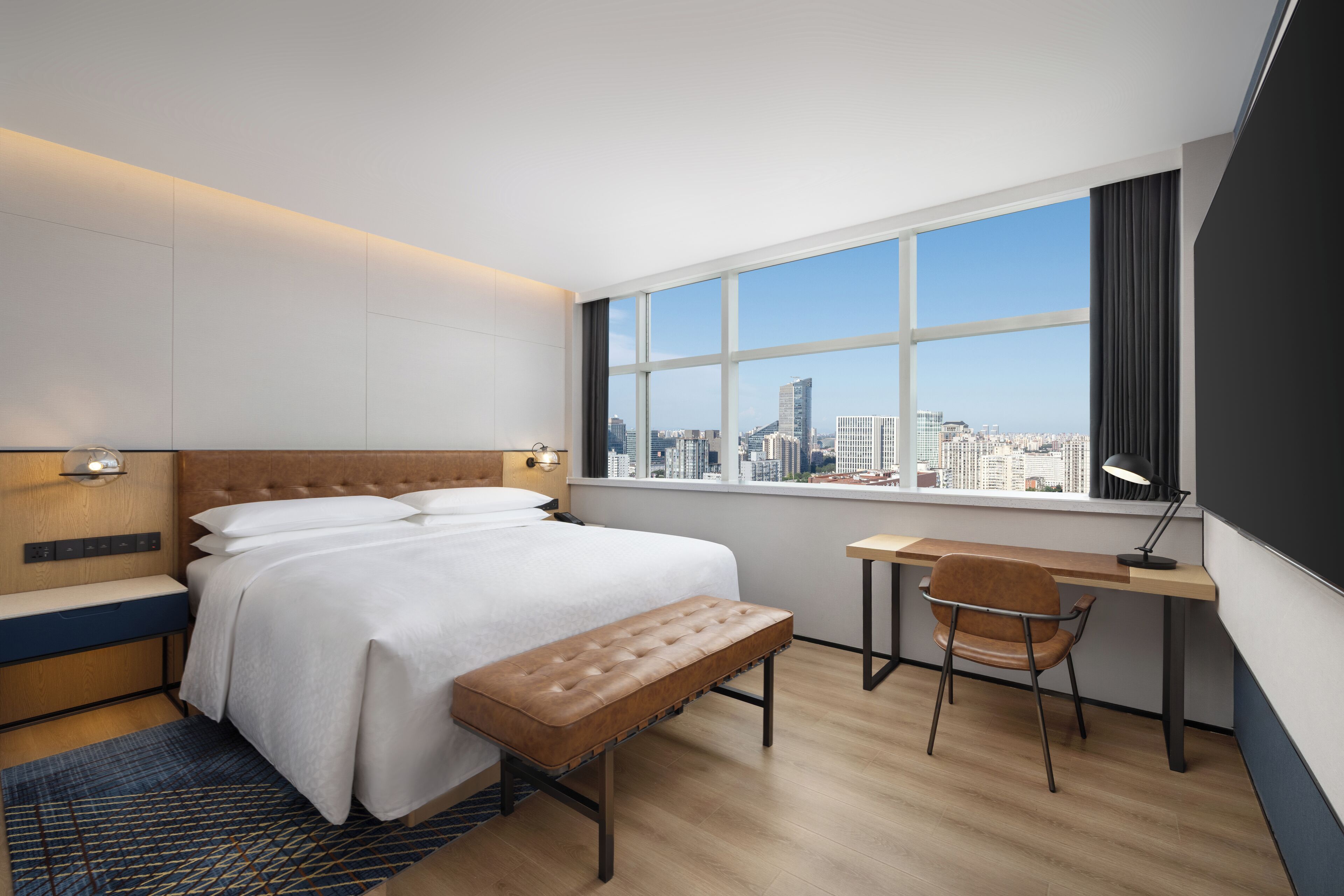 Una habitación de hotel moderna con una cama grande, un escritorio y vistas al horizonte de la ciudad.